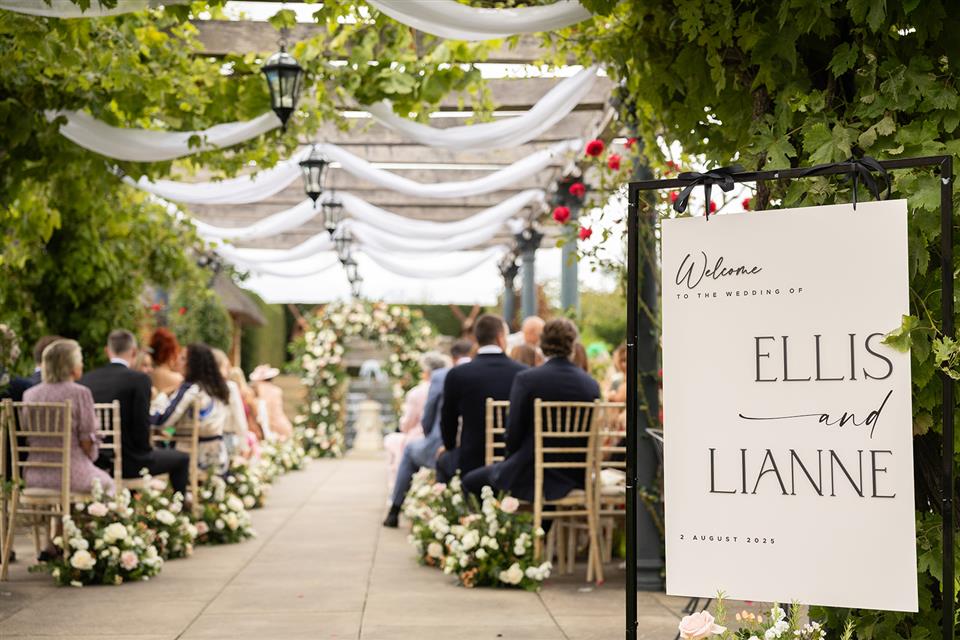 View from the back of the outdoor wedding ceremony with guests seated and flower meadow arrangements down the aisle